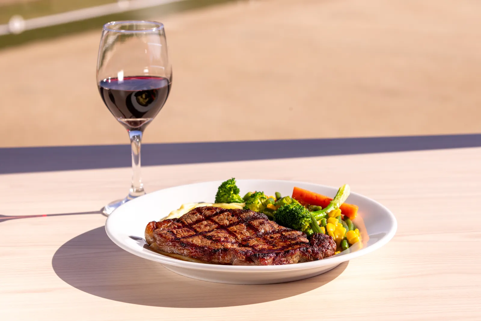 A grilled scotch fillet steak with seasonal vegetables and a glass of red wine