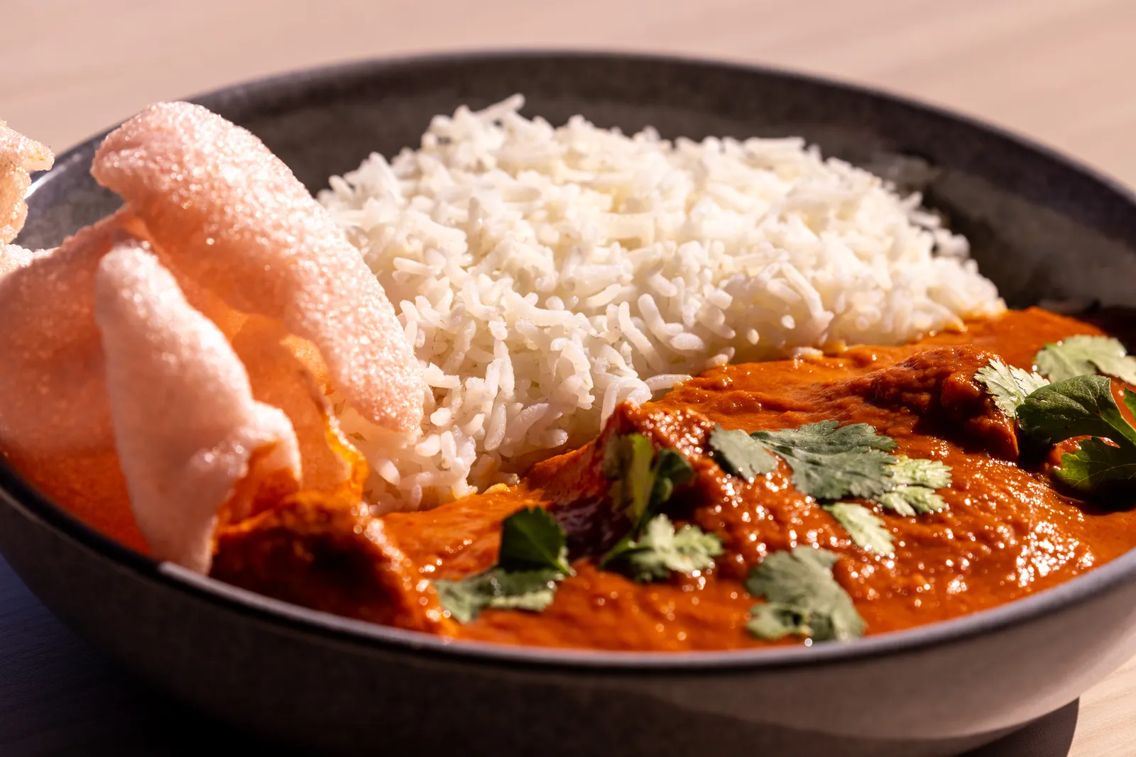 Butter chicken curry with rice and pappadums in a stone bowl