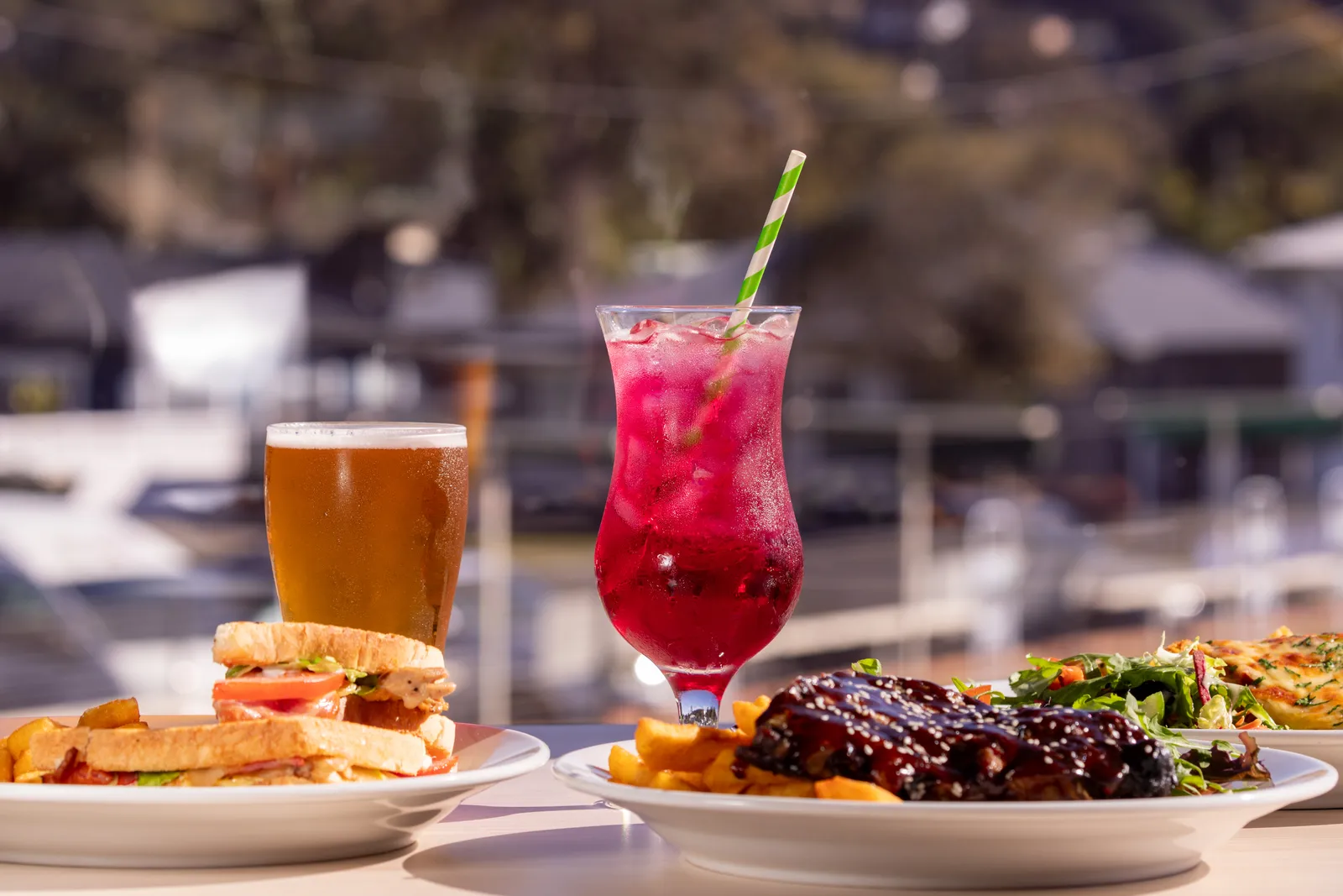 A shared table spread — club sandwich, ribs and a bright berry mocktail
