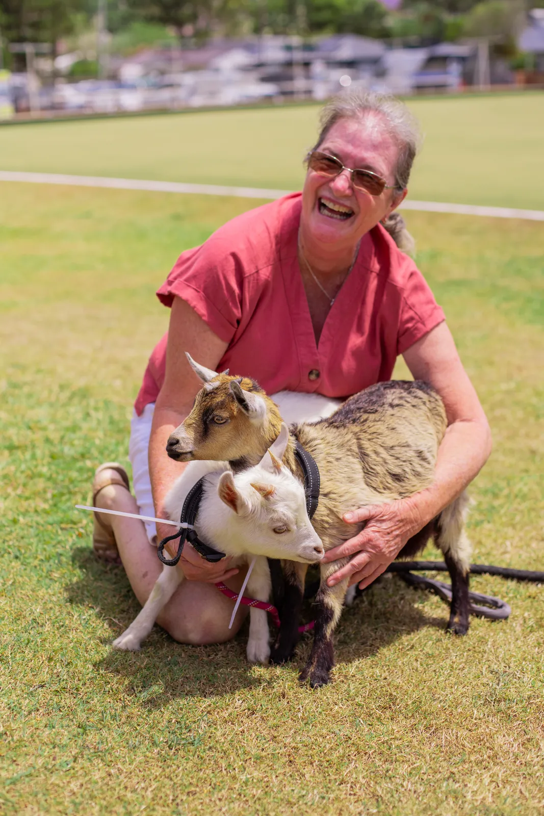A member laughing with two baby goats at a family fun day on the green